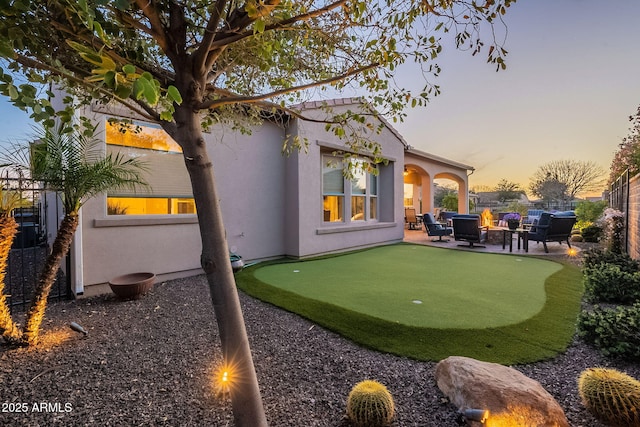 back of property at dusk featuring a patio area, stucco siding, and fence