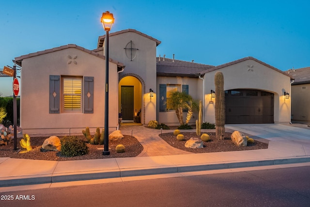 mediterranean / spanish home with stucco siding, an attached garage, driveway, and a tiled roof