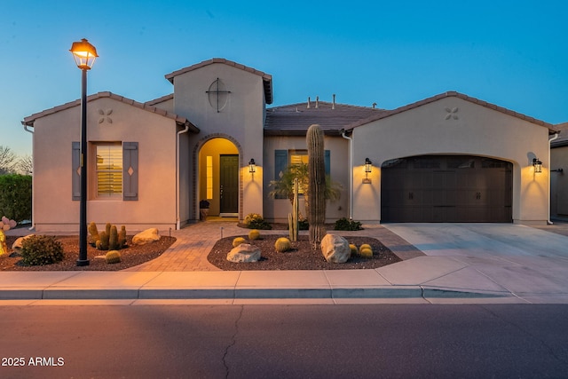 mediterranean / spanish house with a garage, stucco siding, driveway, and a tile roof