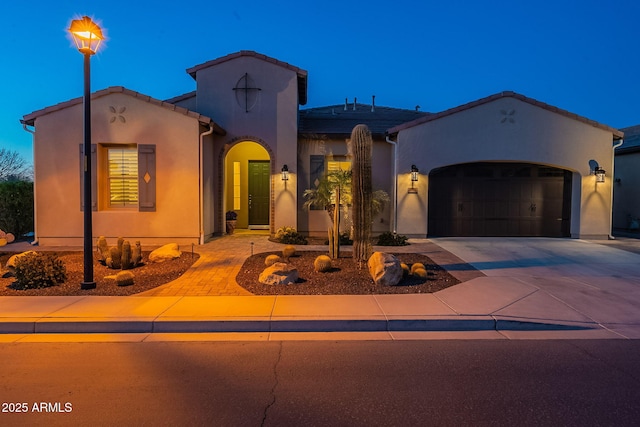 mediterranean / spanish house featuring stucco siding, concrete driveway, an attached garage, and a tiled roof