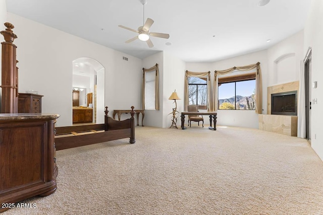 carpeted bedroom featuring visible vents, a ceiling fan, ensuite bathroom, arched walkways, and a fireplace