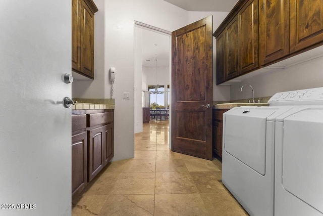 laundry area featuring a sink, cabinet space, an inviting chandelier, and washing machine and clothes dryer