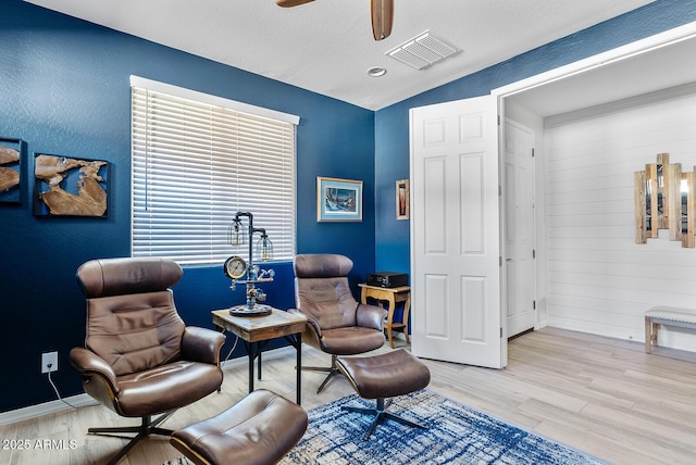 sitting room with light wood finished floors, baseboards, a ceiling fan, and visible vents