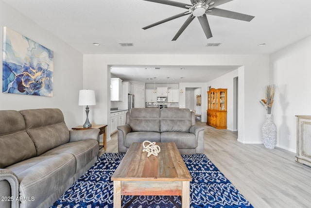 living area with light wood-style flooring, visible vents, a ceiling fan, and baseboards