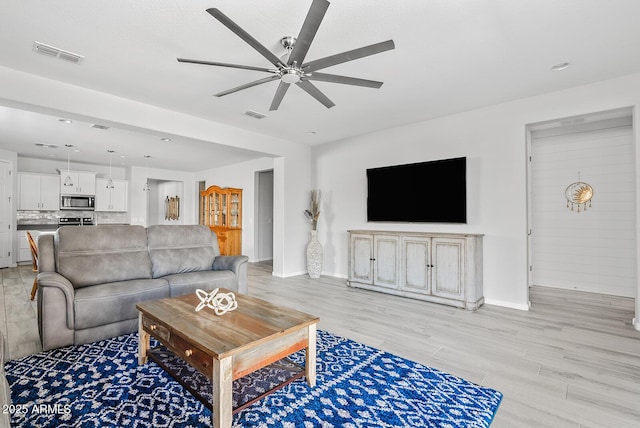 living room featuring light wood-style floors, visible vents, a ceiling fan, and baseboards