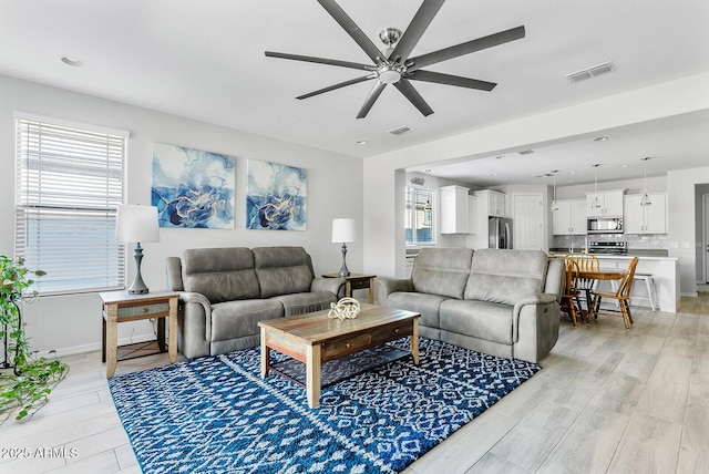 living room featuring baseboards, light wood-style flooring, visible vents, and ceiling fan