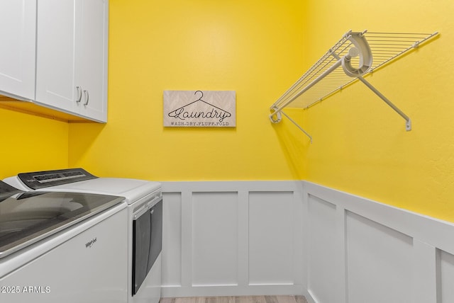 laundry area with a wainscoted wall, light wood-style flooring, cabinet space, separate washer and dryer, and a decorative wall