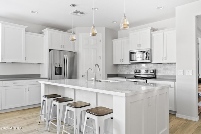 kitchen featuring an island with sink, backsplash, visible vents, a sink, and appliances with stainless steel finishes