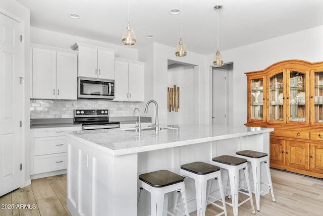 kitchen featuring an island with sink, a sink, light wood-style floors, decorative backsplash, and appliances with stainless steel finishes