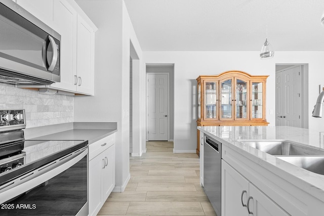 kitchen featuring backsplash, a sink, baseboards, appliances with stainless steel finishes, and white cabinetry