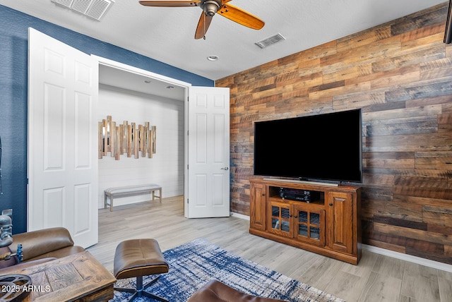 living area featuring wood walls, a ceiling fan, and visible vents