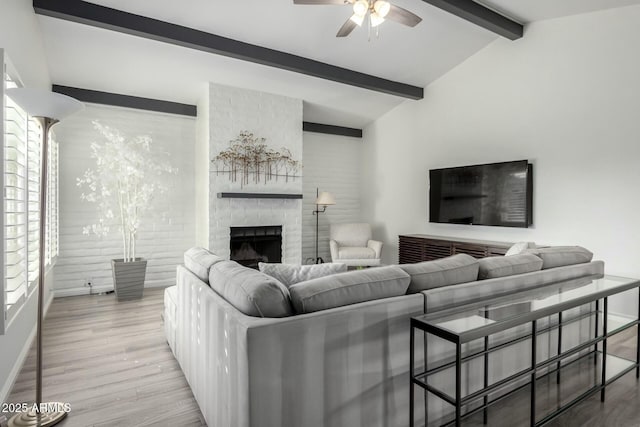 living room with lofted ceiling with beams, ceiling fan, a large fireplace, and light hardwood / wood-style floors