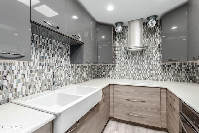 kitchen with sink, light hardwood / wood-style flooring, decorative backsplash, oven, and wall chimney exhaust hood