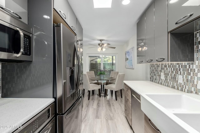 kitchen with sink, decorative backsplash, ceiling fan, stainless steel appliances, and light wood-type flooring