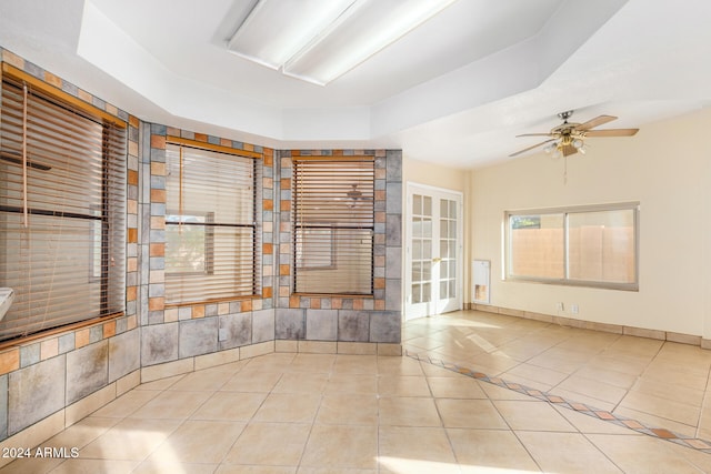 empty room with ceiling fan, light tile patterned floors, and a tray ceiling