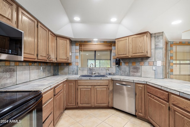 kitchen with tile countertops, sink, stainless steel appliances, and vaulted ceiling