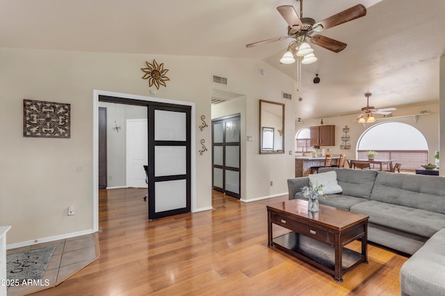 living room with ceiling fan, light hardwood / wood-style floors, and vaulted ceiling