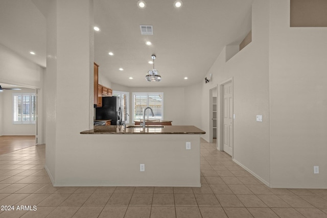 kitchen featuring black refrigerator with ice dispenser, dark stone countertops, decorative light fixtures, sink, and light tile patterned floors