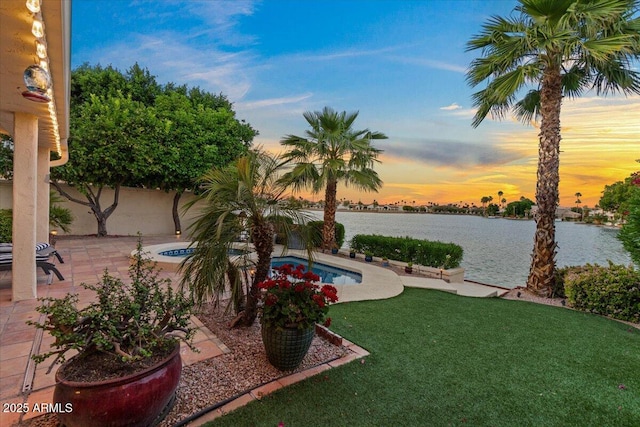 yard at dusk featuring a water view, a patio area, an outdoor pool, and fence