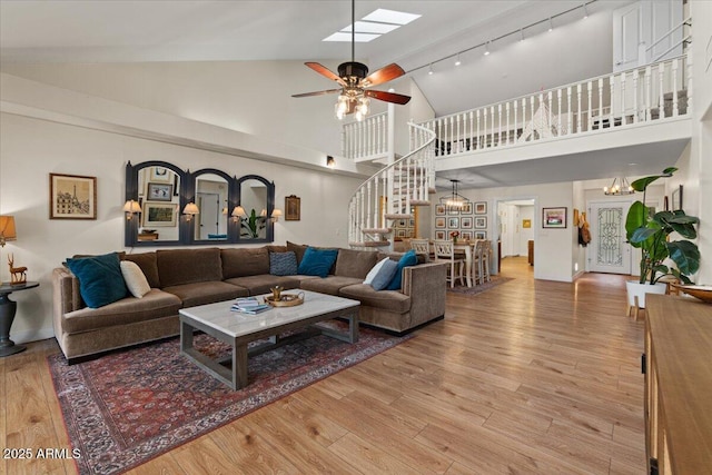 living area featuring stairs, rail lighting, light wood-style flooring, and high vaulted ceiling