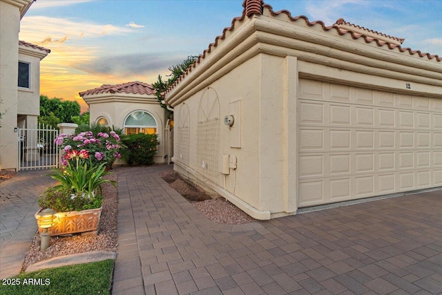 property exterior at dusk featuring a gate, a tiled roof, and stucco siding