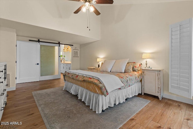 bedroom with a barn door, high vaulted ceiling, ceiling fan, and wood finished floors