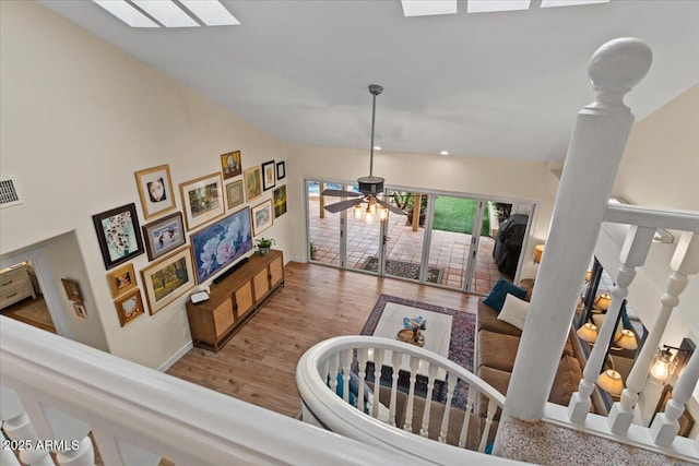 stairs with a ceiling fan, visible vents, wood finished floors, baseboards, and lofted ceiling