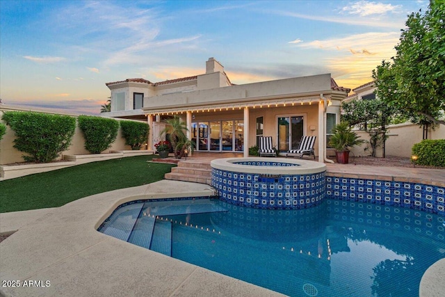 back of house with a pool with connected hot tub, stucco siding, and a chimney