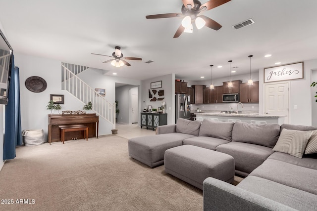 living room featuring light colored carpet, stairway, a ceiling fan, and visible vents