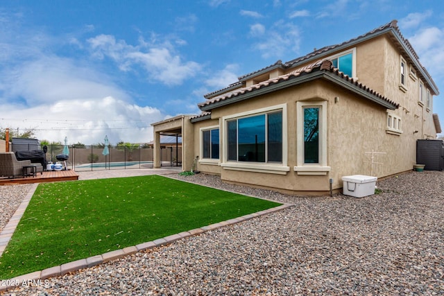 back of house with stucco siding, a lawn, a tile roof, a fenced backyard, and a fenced in pool