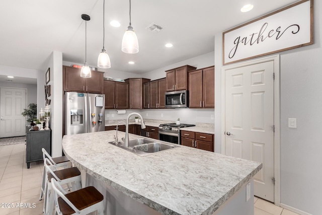 kitchen with light tile patterned floors, a sink, stainless steel appliances, light countertops, and a kitchen bar