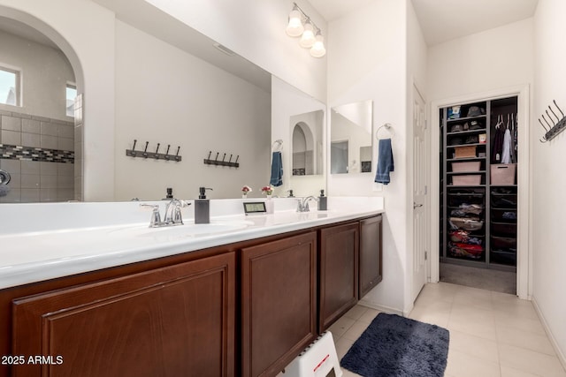 full bath featuring double vanity, a walk in closet, a sink, and tile patterned flooring