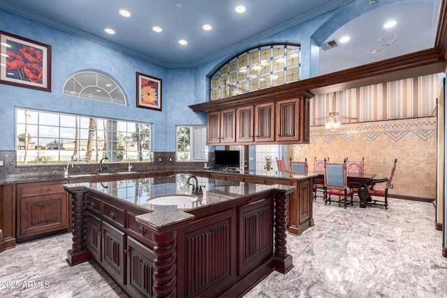 kitchen featuring sink, dark stone counters, a high ceiling, crown molding, and a center island with sink