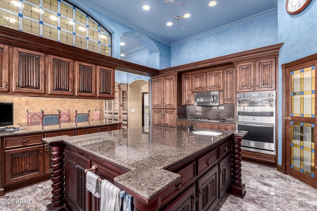 kitchen featuring a kitchen island with sink, crown molding, light stone countertops, and appliances with stainless steel finishes