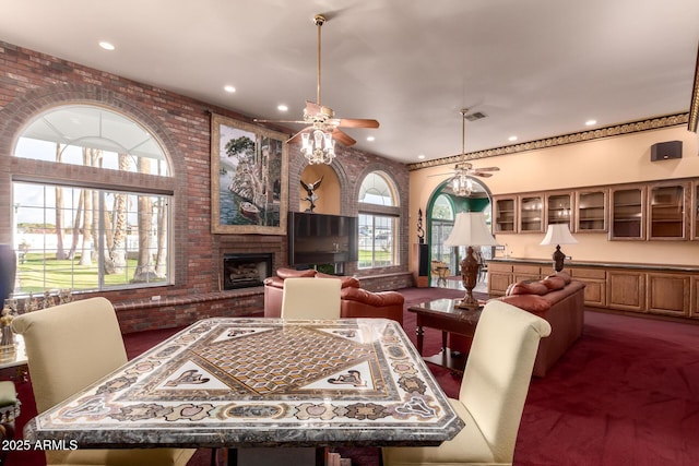 carpeted dining room with ceiling fan, brick wall, a fireplace, and a high ceiling