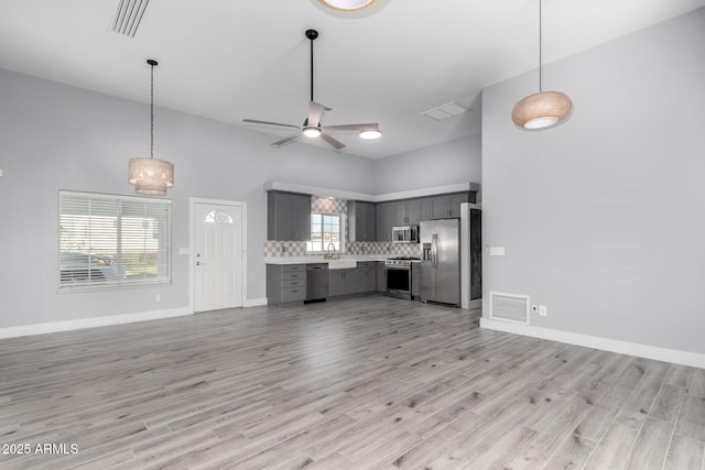 kitchen with light hardwood / wood-style flooring, appliances with stainless steel finishes, gray cabinets, ceiling fan, and backsplash