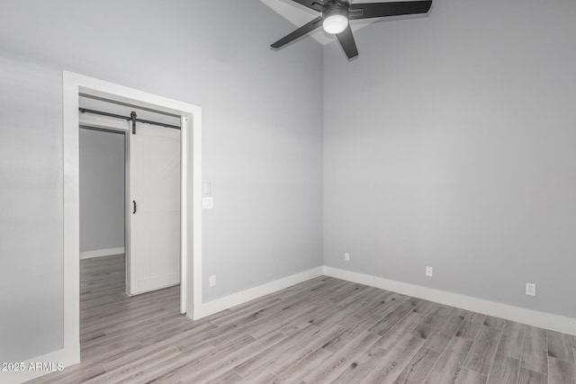 unfurnished bedroom with ceiling fan, a barn door, and light hardwood / wood-style floors