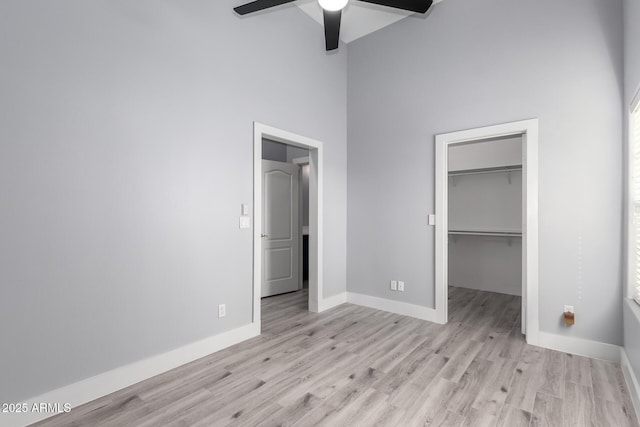 unfurnished bedroom featuring a high ceiling, a spacious closet, ceiling fan, light wood-type flooring, and a closet