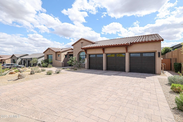 mediterranean / spanish-style house with a residential view, a tile roof, a garage, stucco siding, and decorative driveway