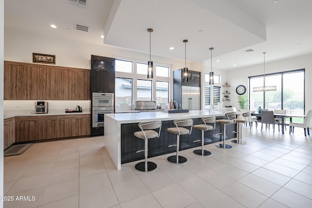 kitchen with a kitchen breakfast bar, visible vents, modern cabinets, brown cabinets, and light countertops
