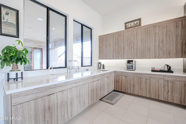 kitchen featuring light brown cabinetry, modern cabinets, light countertops, a sink, and light tile patterned floors
