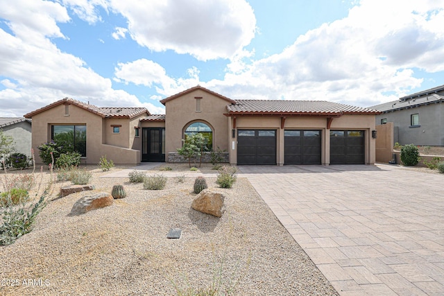 mediterranean / spanish-style home with a tiled roof, decorative driveway, a garage, and stucco siding