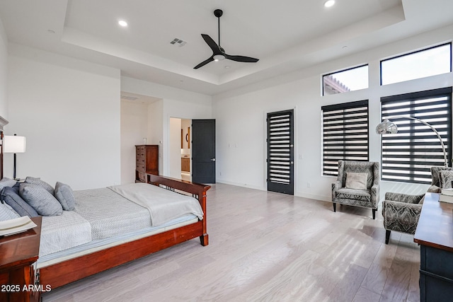 bedroom with a raised ceiling, recessed lighting, wood finished floors, and visible vents