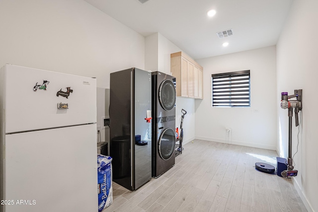 laundry room with baseboards, cabinet space, light wood-type flooring, and stacked washer / dryer