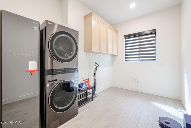 laundry area featuring baseboards, cabinet space, stacked washer and dryer, and light wood-style flooring