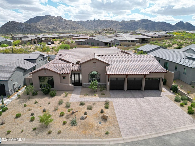 mediterranean / spanish house featuring stucco siding, a tile roof, an attached garage, a mountain view, and a residential view