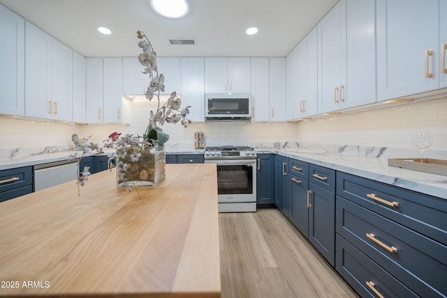 kitchen with stainless steel appliances, blue cabinetry, white cabinets, and light hardwood / wood-style flooring