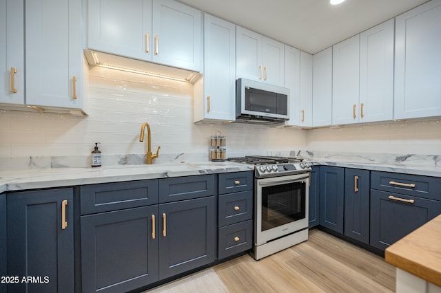 kitchen featuring sink, backsplash, stainless steel gas range oven, white cabinets, and light wood-type flooring