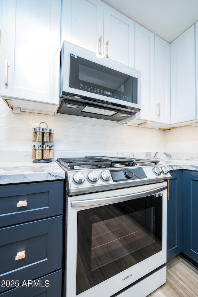 kitchen with blue cabinetry, stainless steel gas range, white cabinetry, light stone counters, and decorative backsplash