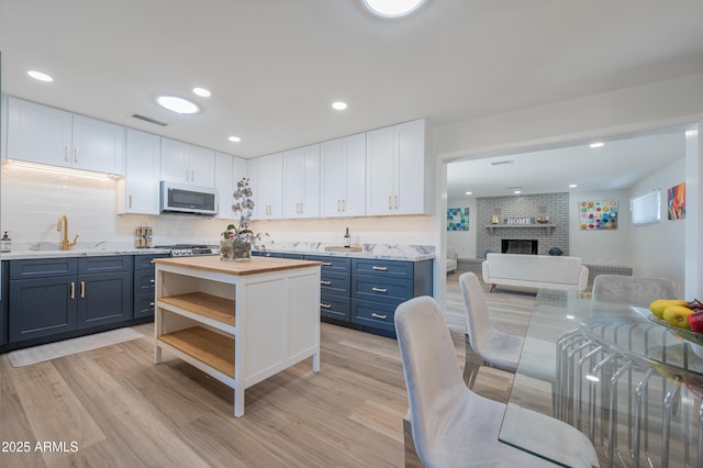 kitchen featuring a brick fireplace, light hardwood / wood-style floors, white cabinets, and blue cabinets